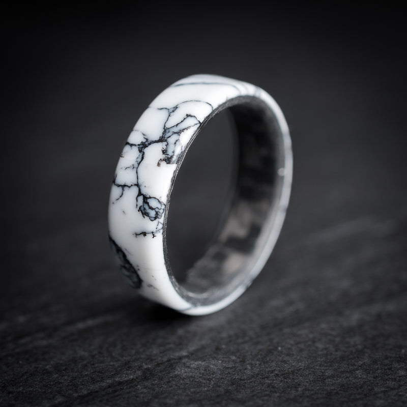 A unisex white and black TruStone ring with a carbon fiber core, displayed on a dark textured surface.